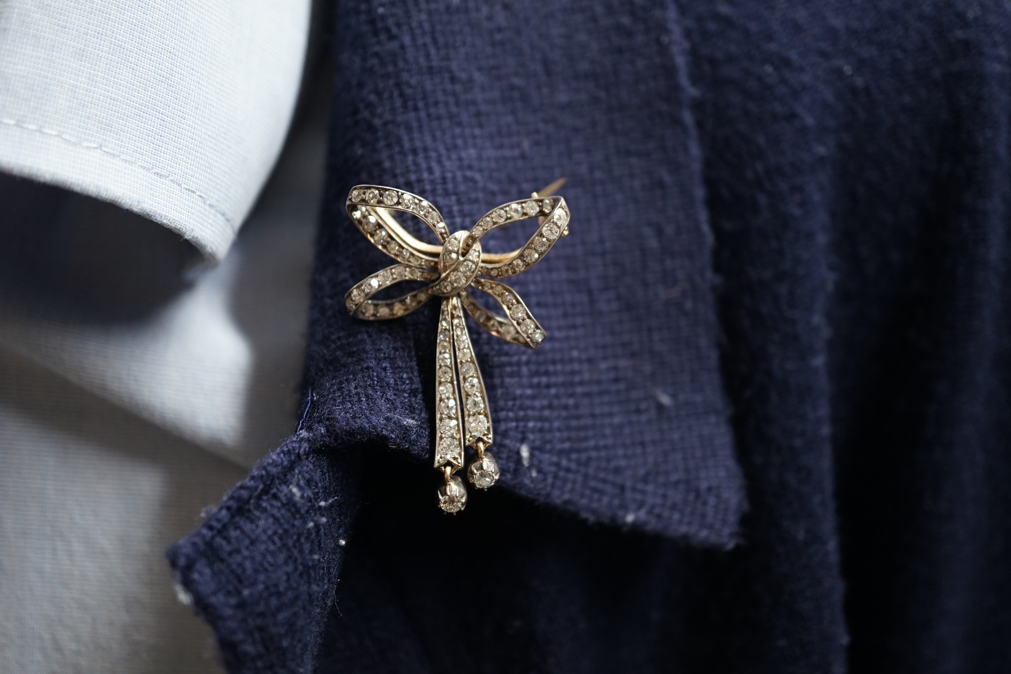 An Edwardian gold, silver and graduated diamond cluster set twin drop ribbon bow brooch